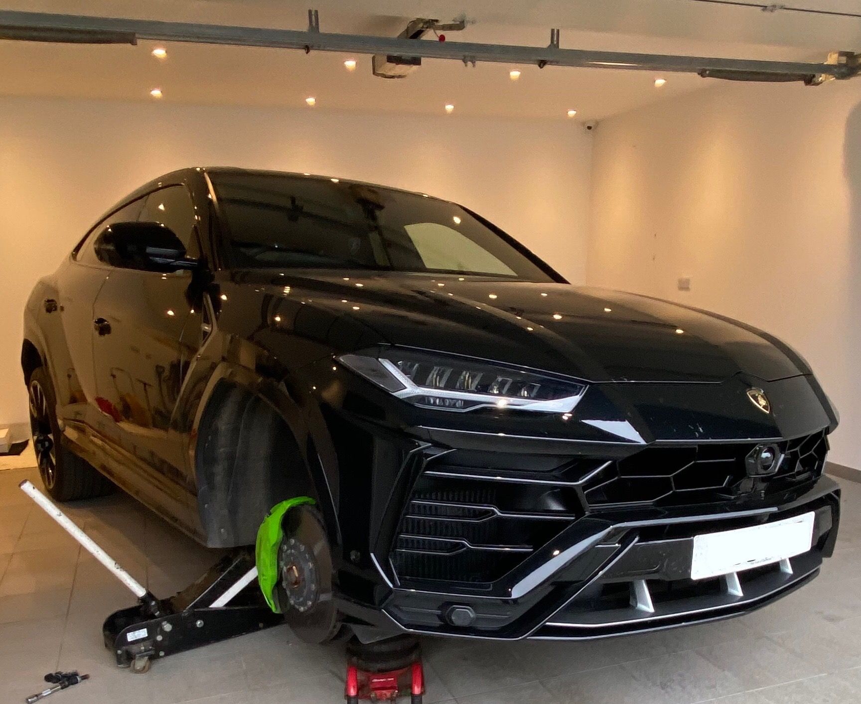 Black Lamborghini Urus on a trolley jack in a home garage with a front wheel off
