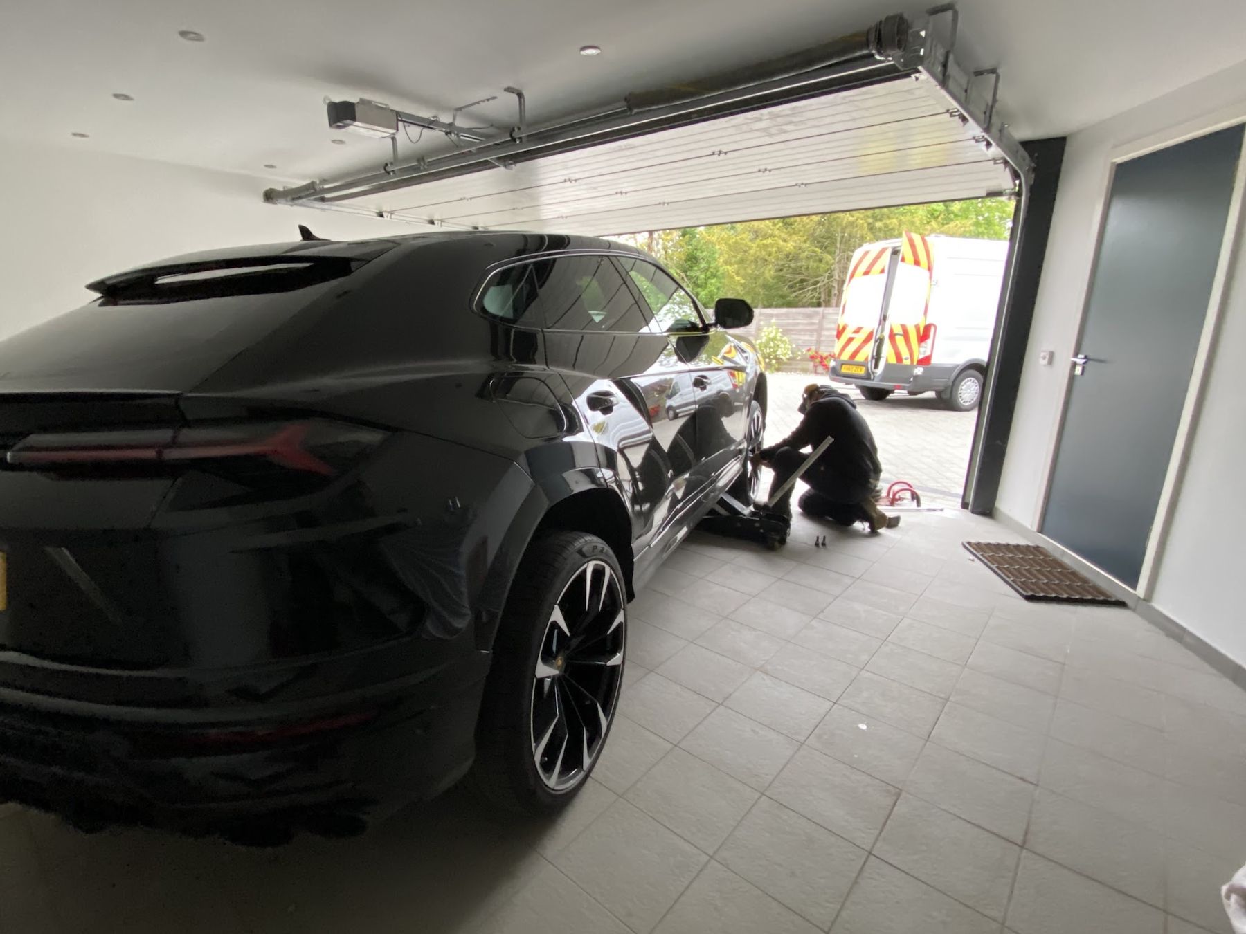 Fitter working on a wheel of a Lamborghini Urus inside a garage, van parked outside