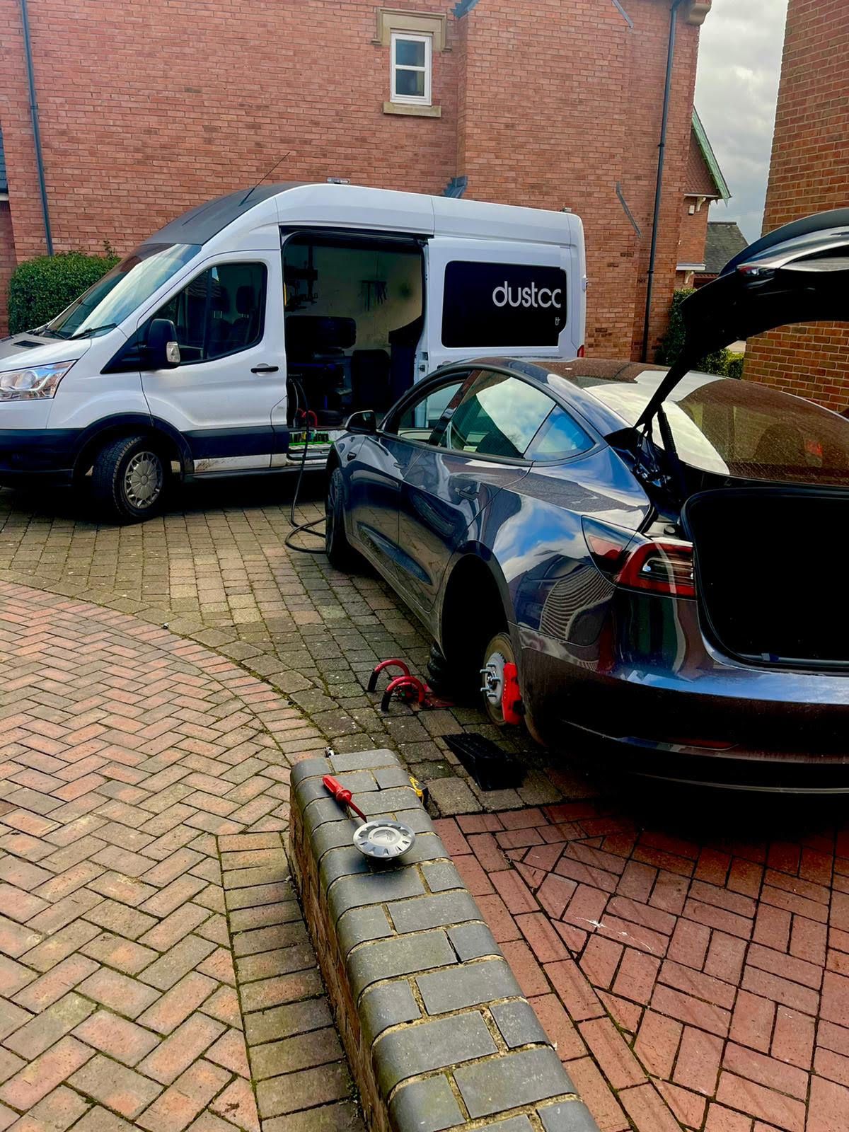 Our white Dustcap van with the side door open showing the workshop inside, parked beside a Tesla on a block-paved drive