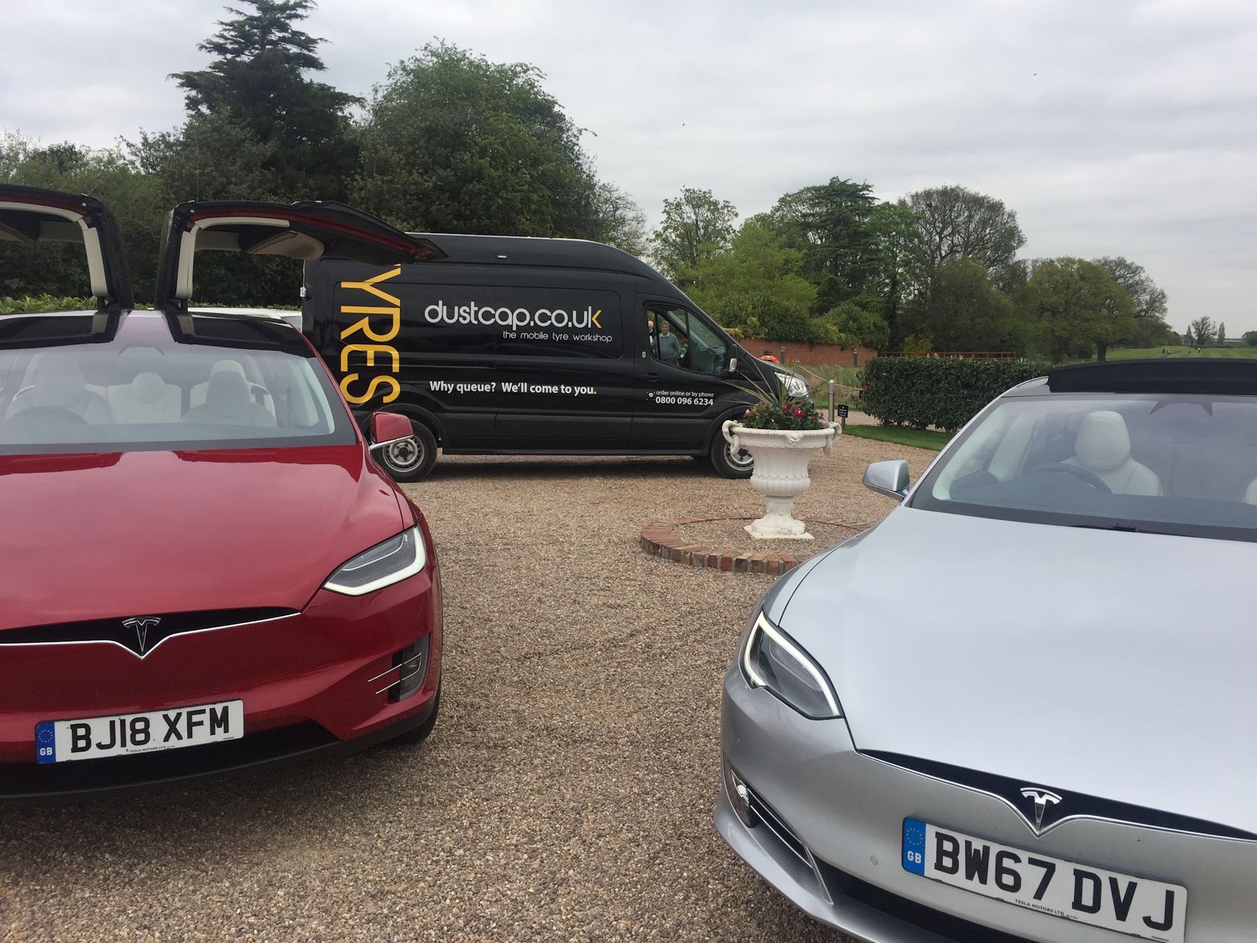 Our black Dustcap van parked on a country house gravel drive beside two Teslas